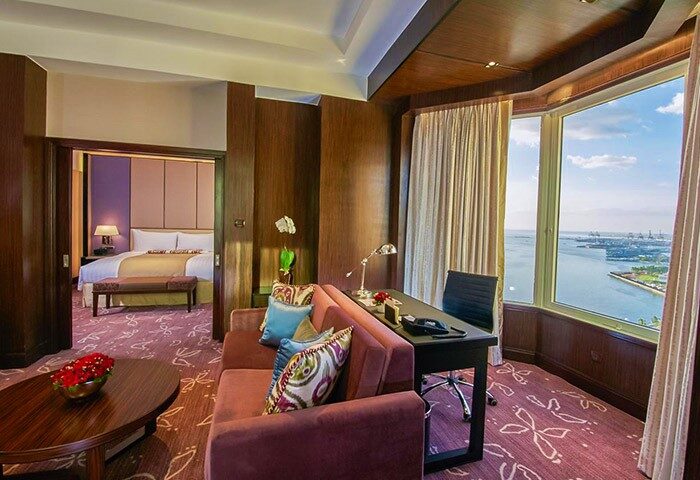 Diamond Hotel gay-friendly suite. Living area with sofa, desk, and ocean view. Bedroom visible through doorway. Luxury gay travel.