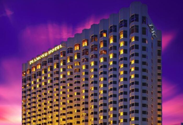 Exterior of Diamond Hotel, a gay-friendly hotel. High-rise building with many windows against a colorful sunset sky. DSC logo on top.