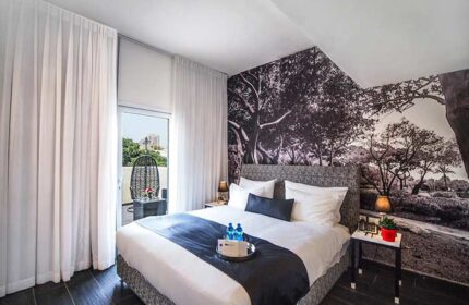 Gay-Friendly Dizengoff Avenue Boutique Hotel room. Balcony view, tree wallpaper, bed with blue runner. Modern, stylish design for gay travelers.