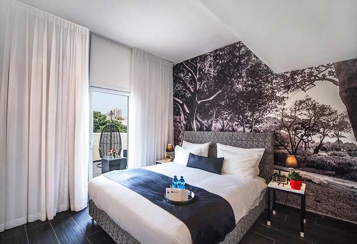 Gay-Friendly Dizengoff Avenue Boutique Hotel room. Balcony view, tree wallpaper, bed with blue runner. Modern, stylish design for gay travelers.