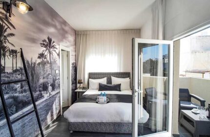 Gay-friendly Dizengoff Avenue Boutique Hotel room. Balcony view, bed, and beach mural. Ideal for gay travel in Tel Aviv, Israel.