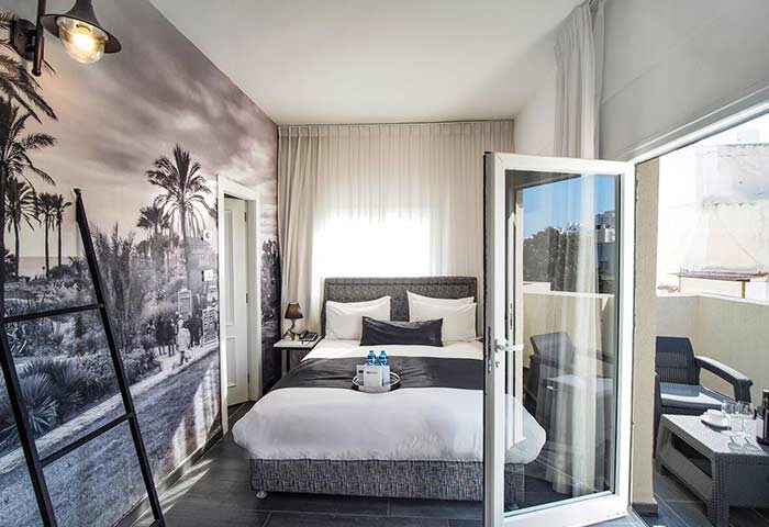 Gay-friendly Dizengoff Avenue Boutique Hotel room. Balcony view, bed, and beach mural. Ideal for gay travel in Tel Aviv, Israel.