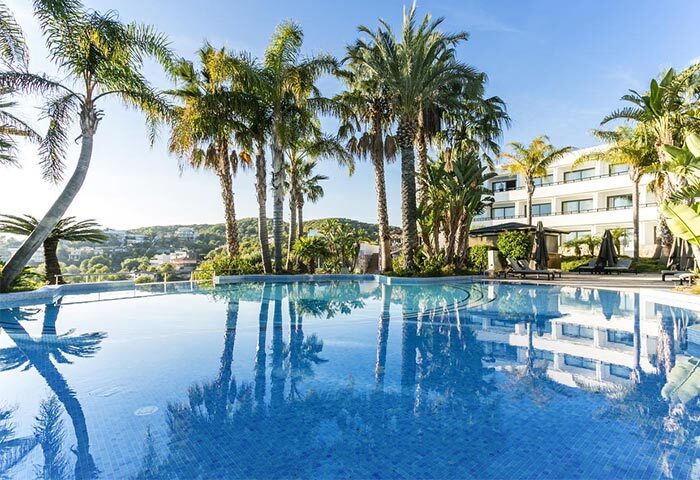 Dolce by Wyndham Sitges gay-friendly hotel pool. Palm trees reflect in the water. A relaxing gay travel destination in Spain.