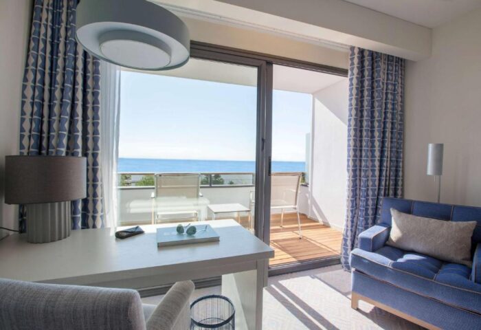 Dolce by Wyndham Sitges gay-friendly hotel room. Ocean view from balcony. Desk, blue sofa, and stylish decor. Gay travel in Sitges.