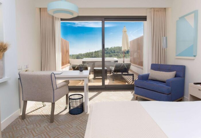 Dolce by Wyndham Sitges gay-friendly hotel room. Balcony with jacuzzi, desk, and blue armchair. Modern design, ideal for gay travelers.