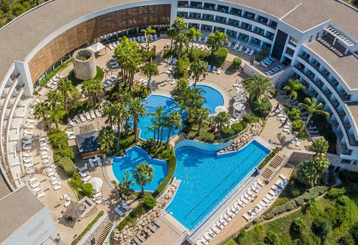 Aerial view of Dolce by Wyndham Sitges, a gay-friendly hotel. Pools, palm trees, and sun loungers create a relaxing resort atmosphere.
