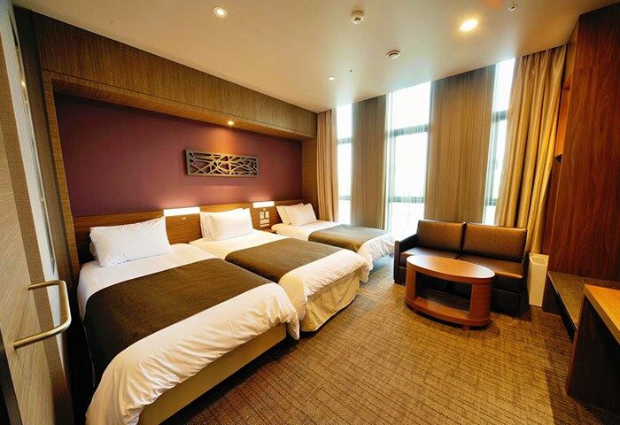 Dormy Inn Premium Seoul Garosugil hotel room. Three beds, sofa, and table. Gay-friendly hotel in Seoul, South Korea.