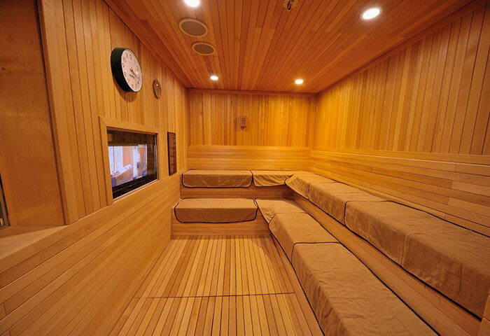 Sauna at Dormy Inn Premium Seoul Garosugil, a gay-friendly hotel. Wood paneled interior, tiered seating, clock, & small window. Relaxation.