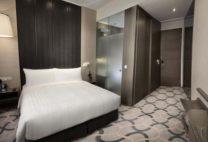 Dorsett Singapore hotel room. Gay-friendly hotel featuring a bed with white linens, modern decor, and a stylish carpet. Great for gay travel.