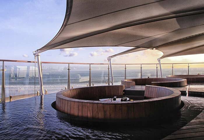 Double-Six Luxury Hotel Seminyak's gay-friendly rooftop bar. Wooden seating areas are partially submerged in water, overlooking the sea.