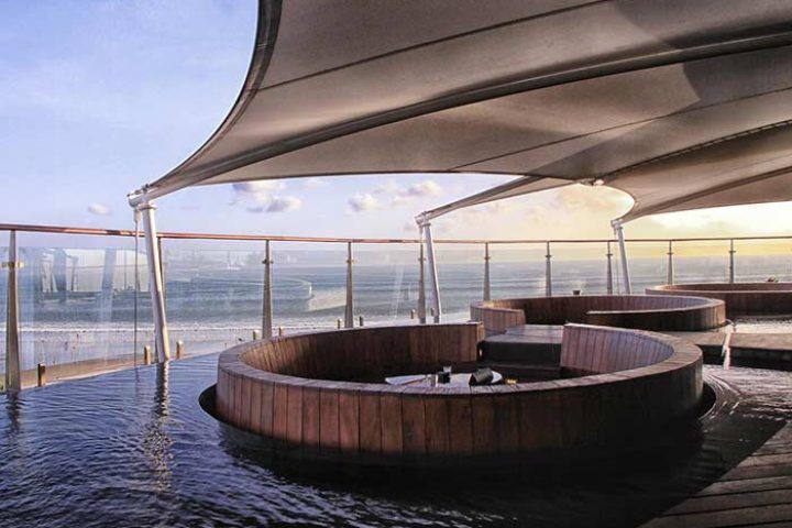 Double-Six Luxury Hotel Seminyak's gay-friendly rooftop bar. Wooden seating areas are partially submerged in water, overlooking the sea.