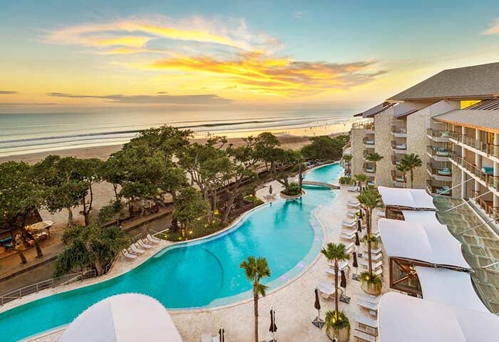 Double-Six Luxury Hotel Seminyak pool view. Gay-friendly hotel with beach access, palm trees, and ocean sunset. Ideal for gay travel.