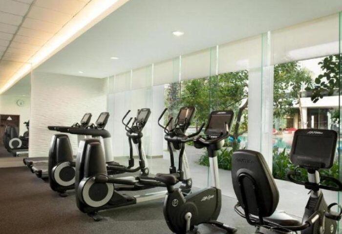 Gym at DoubleTree by Hilton Hotel Jakarta Diponegoro, a gay-friendly hotel. Treadmills and exercise bikes face windows overlooking the pool.