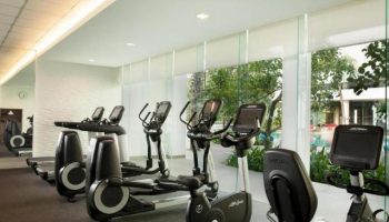 Gym at DoubleTree by Hilton Hotel Jakarta Diponegoro, a gay-friendly hotel. Treadmills and exercise bikes face windows overlooking the pool.