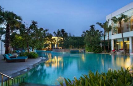 DoubleTree by Hilton Hotel Jakarta Diponegoro pool at dusk. Gay-friendly hotel with palm trees, lounge chairs, and inviting turquoise water.