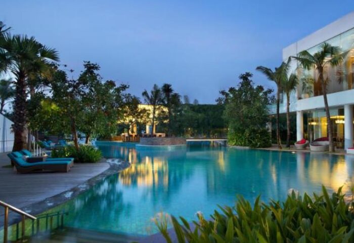 DoubleTree by Hilton Hotel Jakarta Diponegoro pool at dusk. Gay-friendly hotel with palm trees, lounge chairs, and inviting turquoise water.