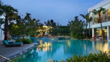 DoubleTree by Hilton Hotel Jakarta Diponegoro pool at dusk. Gay-friendly hotel with palm trees, lounge chairs, and inviting turquoise water.
