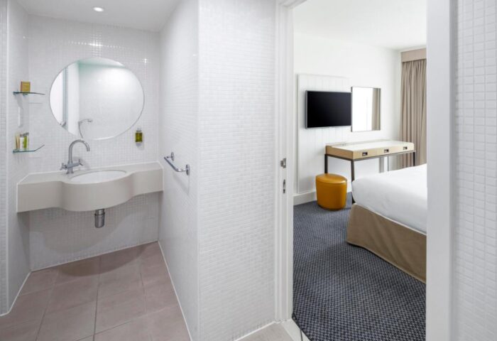 DoubleTree by Hilton Manchester Piccadilly gay-friendly hotel: Bathroom with sink, round mirror. Bedroom with TV, desk, stool. Modern, clean design.