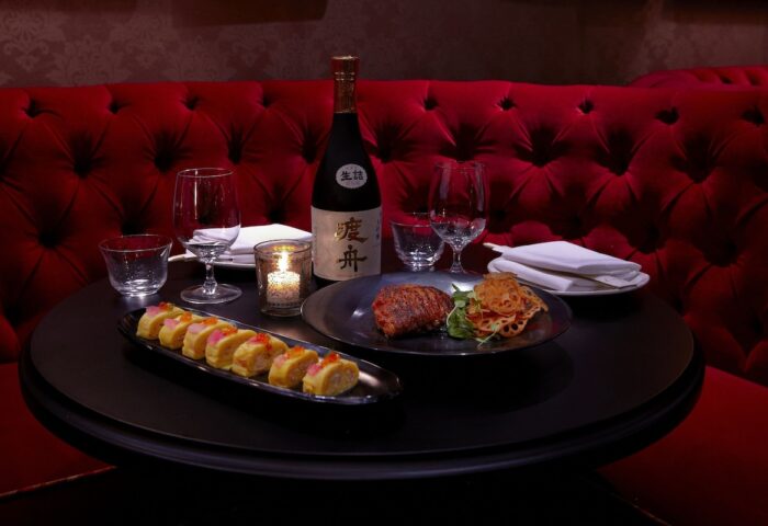 Fine dining at Dream Downtown Hotel, a gay-friendly hotel. Sushi, steak, and sake on a table with a red tufted booth. Romantic dinner.