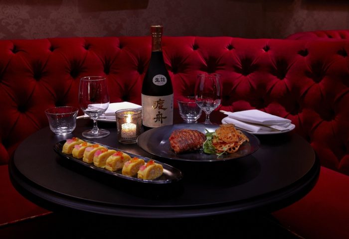 Fine dining at Dream Downtown Hotel, a gay-friendly hotel. Sushi, steak, and sake on a table with a red tufted booth. Romantic dinner.