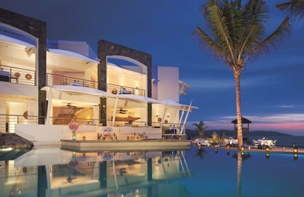 Dreams Vallarta Bay Resort & Spa all-inclusive, gay-friendly hotel. Poolside bar and dining at dusk. Palm tree, ocean view. Luxury travel.