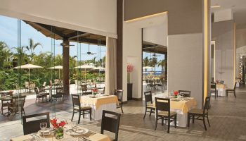Dreams Vallarta Bay Resort & Spa all-inclusive dining. Restaurant interior with tables set, view to outdoor patio. Gay-friendly hotel.