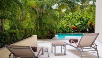 Dreams Vallarta Bay Resort & Spa all-inclusive, gay-friendly hotel. Two lounge chairs face a pool surrounded by lush tropical plants.