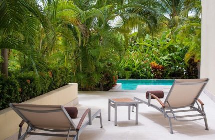 Dreams Vallarta Bay Resort & Spa all-inclusive, gay-friendly hotel. Two lounge chairs face a pool surrounded by lush tropical plants.