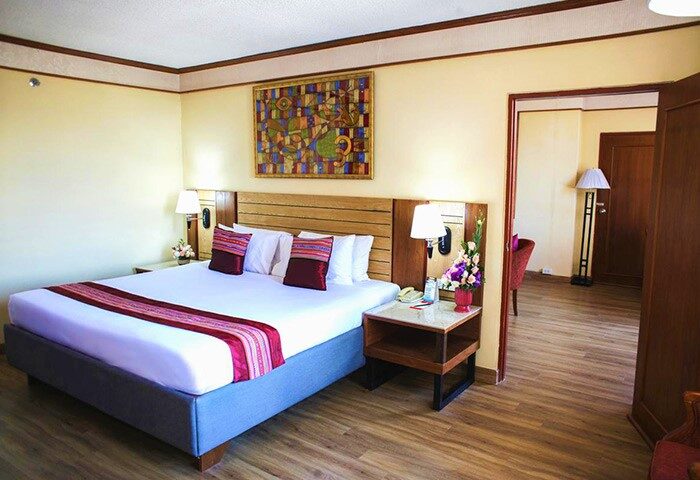 Duangtawan Hotel Chiang Mai room. Gay-friendly hotel bedroom with a large bed, colorful artwork, and a view into an adjacent sitting area.