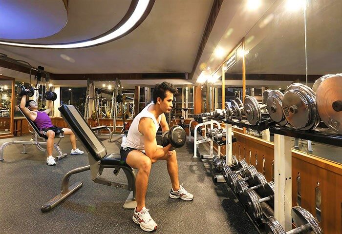 Duangtawan Hotel gym: Two men lifting weights. Gay-friendly hotel with fitness center in Chiang Mai, Thailand. Exercise equipment.