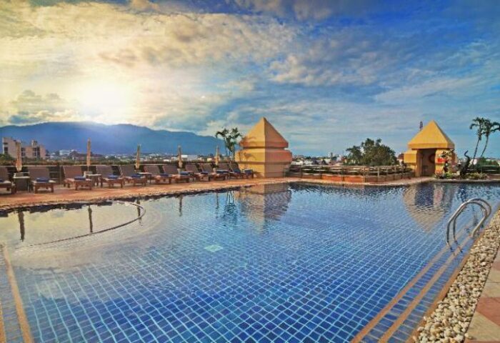Duangtawan Hotel Chiang Mai rooftop pool view. Gay-friendly hotel with sun loungers, city skyline, and mountain backdrop. Perfect for gay travel.