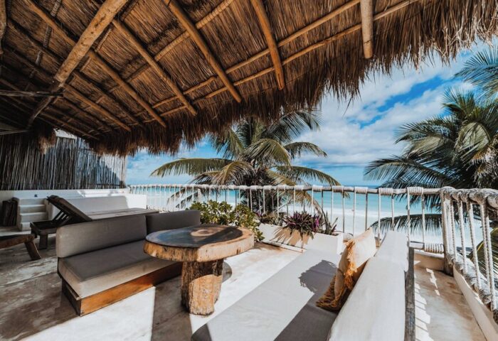 Dune Boutique Hotel's gay-friendly party zone: terrace view. Thatched roof, ocean vista, stylish outdoor furniture. Tropical paradise vibes.