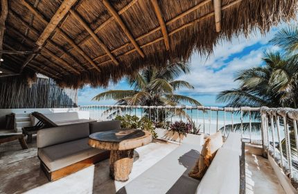 Dune Boutique Hotel's gay-friendly party zone: terrace view. Thatched roof, ocean vista, stylish outdoor furniture. Tropical paradise vibes.