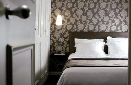 Gay-Friendly Hotel Duo Hotel bedroom. Bed with white linens, floral wallpaper, and a door ajar. Interior design of a gay hotel room.