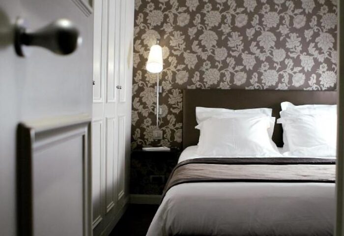 Gay-Friendly Hotel Duo Hotel bedroom. Bed with white linens, floral wallpaper, and a door ajar. Interior design of a gay hotel room.