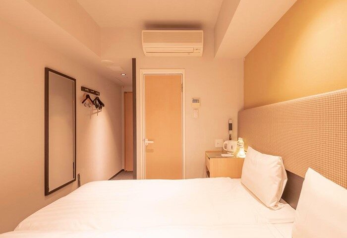 E-Hotel Higashi Shinjuku, Tokyo room. Gay-friendly hotel featuring a bed, nightstand, mirror, and air conditioner. Clean, modern design.