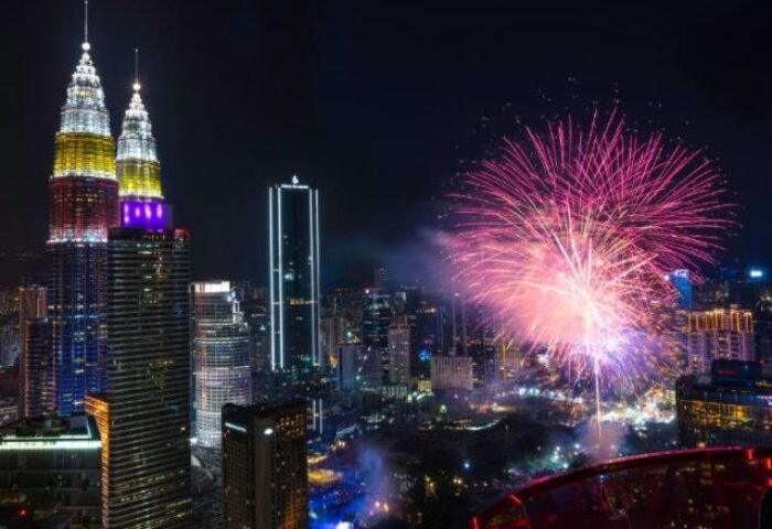Night view of EQ Kuala Lumpur, a gay-friendly hotel, with fireworks over the city skyline and Petronas Towers. A vibrant travel destination.