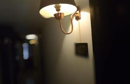 Illuminated wall lamp at East Hotel, a gay-friendly hotel. The lamp has a dark shade and a copper-colored arm, providing warm lighting.