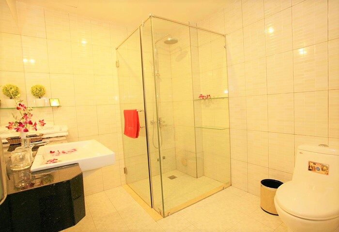 Bathroom at Eclipse Legend Hotel, a gay-friendly hotel. Features a glass shower, sink with flowers, and toilet. Great for gay men travel.