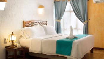Eco-hotel El Rey del Caribe room. Gay-friendly hotel with bed, swan towel art, blue curtains, and bedside table. Gay travel lodging.