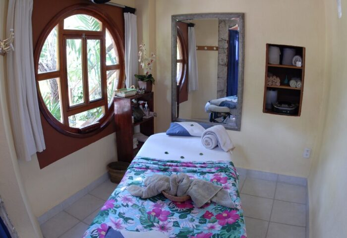 Eco-hotel El Rey del Caribe spa. Gay-friendly hotel massage table with floral blanket, round window, mirror, shelves. Relaxation & wellness.