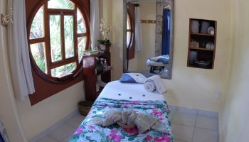 Eco-hotel El Rey del Caribe spa. Gay-friendly hotel massage table with floral blanket, round window, mirror, shelves. Relaxation & wellness.