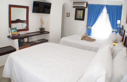Eco-hotel El Rey del Caribe gay-friendly room. Two beds with white linens, blue curtains, TV, safe. Gay travel in a comfortable hotel.