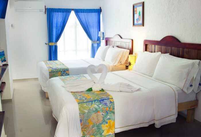 Eco-hotel El Rey del Caribe gay-friendly room. Two beds, white linens, swan towels, blue curtains. Gay travel in Playa del Carmen.