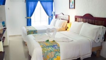 Eco-hotel El Rey del Caribe gay-friendly room. Two beds, white linens, swan towels, blue curtains. Gay travel in Playa del Carmen.