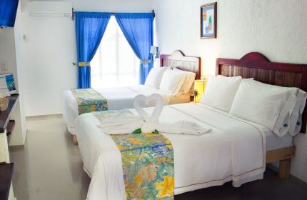 Eco-hotel El Rey del Caribe gay-friendly room. Two beds, white linens, swan towels, blue curtains. Gay travel in Playa del Carmen.