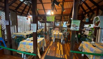 Dining area at El Rey del Caribe, a gay-friendly eco-hotel. Tables with patterned cloths under a wooden roof. A welcoming space for gay travelers.