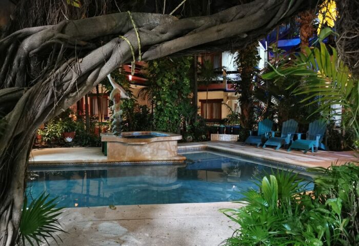 Eco-hotel El Rey del Caribe pool area at night. Gay-friendly hotel with lush greenery, pool, and chairs. Ideal for gay men's travel.