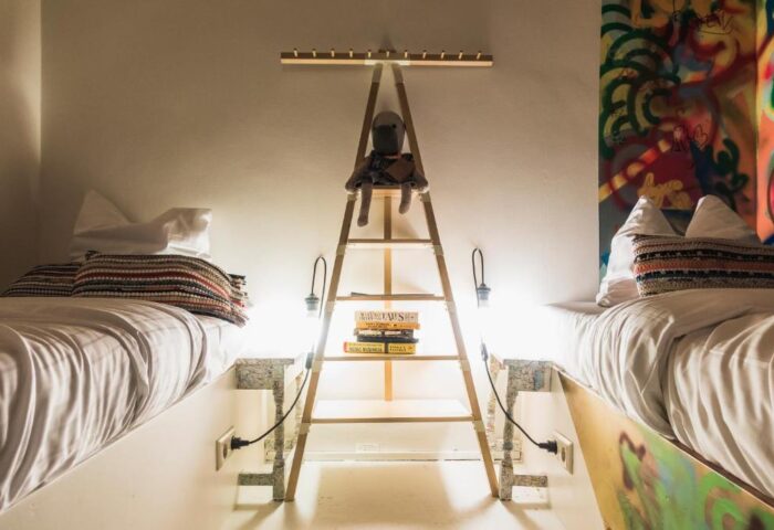 Ecomama Hotel's gay-friendly room: twin beds, ladder nightstand with a doll, books, & lamps. Graffiti art adds flair to this unique hotel room.