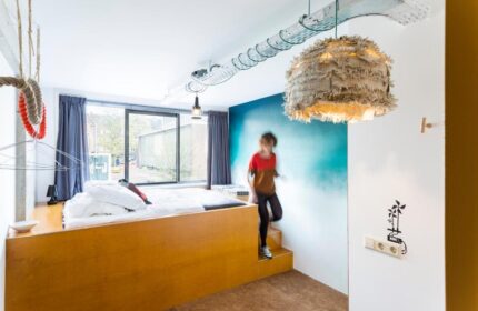 Ecomama Hotel room with raised bed, unique lighting, and a person descending steps. Gay-friendly hotel design for modern travelers.